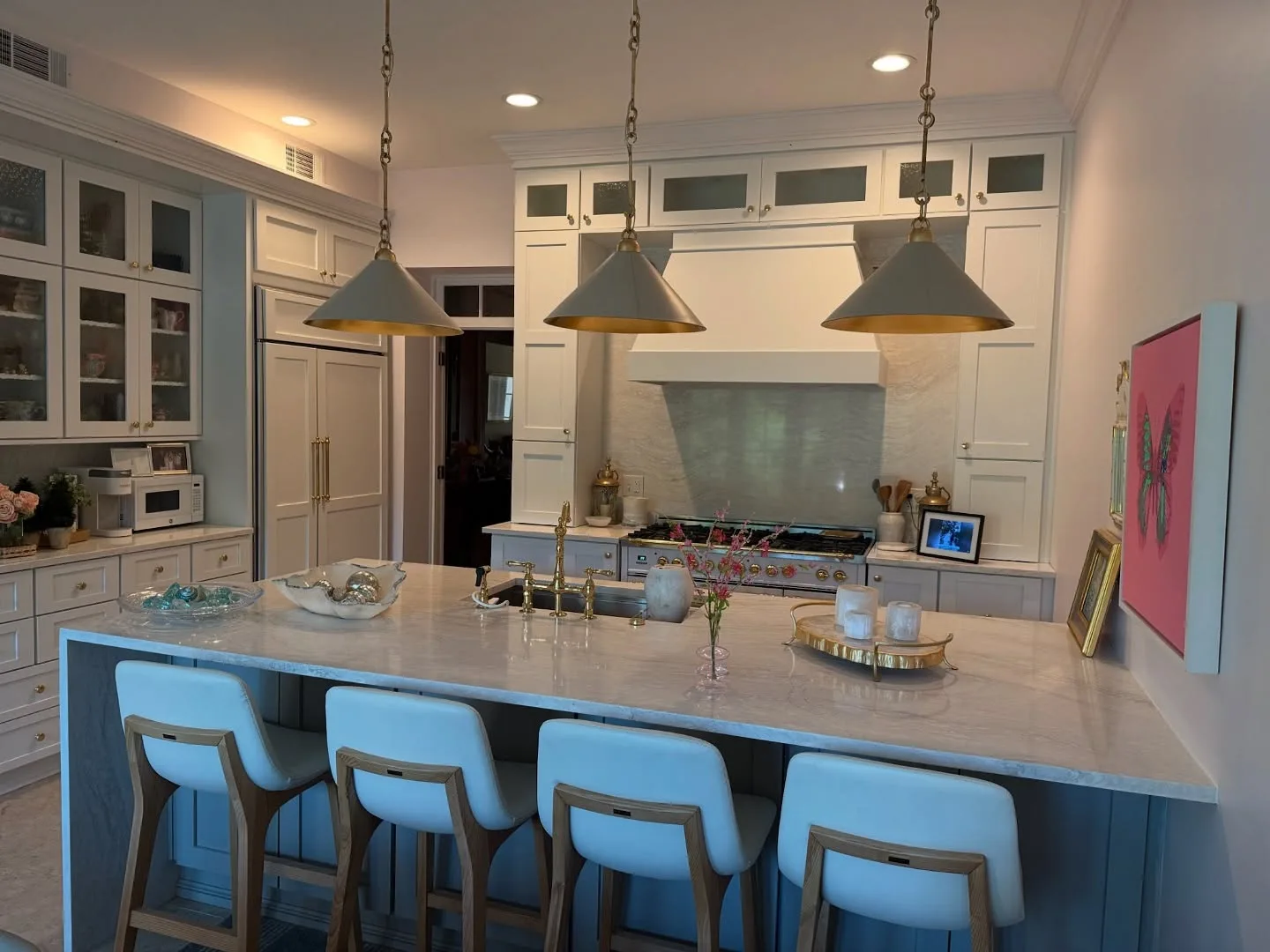 A kitchen with a waterfall quartz island, brass pendant lights and custom white cabinetry